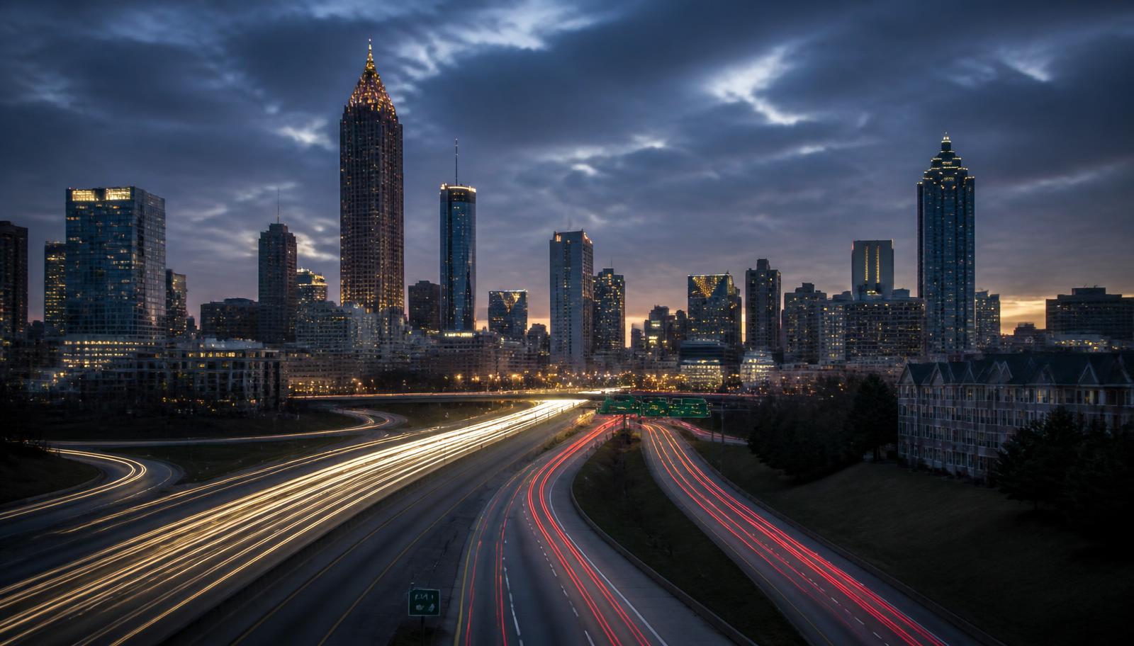 City skyline at dusk seen from a highway with traffic light trails